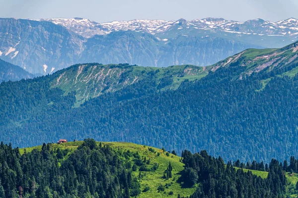 Green mountain ridges, surrounded by high mountains. Snow-capped mountain peaks on the horizon. Krasnaya Polyana, Sochi, Caucasus, Russia.