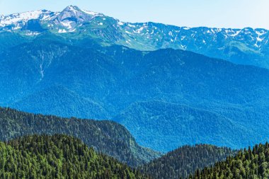 Yeşil dağ sırtları, yüksek dağlarla çevrili. Ufukta karla kaplı dağ zirveleri. Krasnaya Polyana, Soçi, Kafkasya, Rusya Federasyonu.