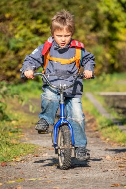 Küçük çocuk sonbahar parkında bisiklet sürüyor..