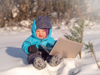 Küçük bir çocuk laptopuyla karda oturuyor..