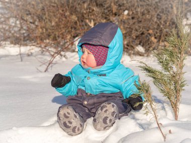 Küçük bir çocuk parkta karda oturuyor.