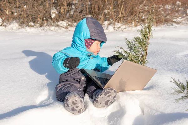 Маленький ребенок сидит в снегу с ноутбуком . — стоковое фото