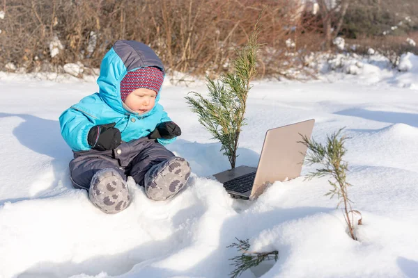 Un bambino piccolo si siede nella neve con un computer portatile . — Foto Stock