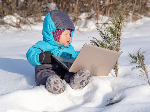 Un bambino piccolo si siede nella neve con un computer portatile . — Foto Stock