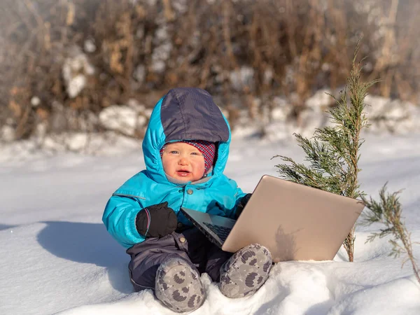 Un bambino piccolo si siede nella neve con un computer portatile . — Foto Stock