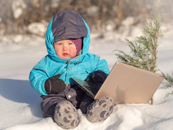 Ein kleines Kind sitzt mit einem Laptop im Schnee. — Stockfoto