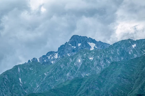 High mountains with snowy peaks at sunset in clouds and fog. High mountains with green slopes and snowy peaks. Mountain ranges in summer