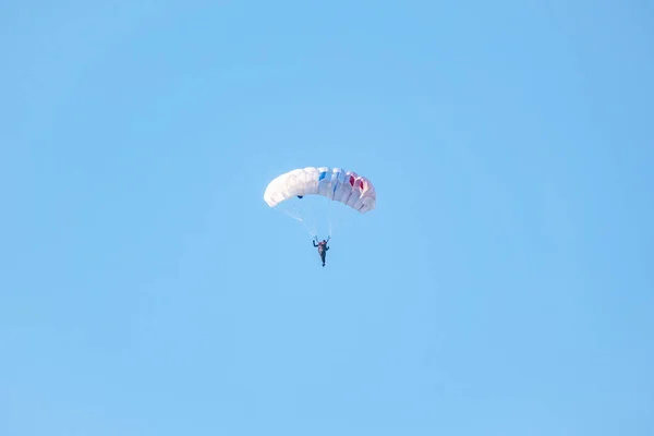 一个带着白色降落伞的跳伞运动员在晴朗天空的背景下缓慢地在低空飞行 运动和积极的极端放松 — 图库照片