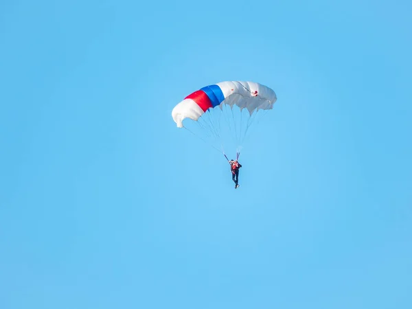 白いパラシュートを持つパラシュートの1つは 澄んだ空の背景に低い高度でゆっくりと浮かんでいます スカイダイビング スポーツや極端なリラクゼーションのアクティブな種類 — ストック写真