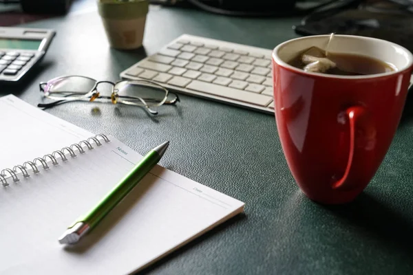 工作场所 可欣赏键盘 笔记本 旧眼镜和带茶水的红杯 — 图库照片