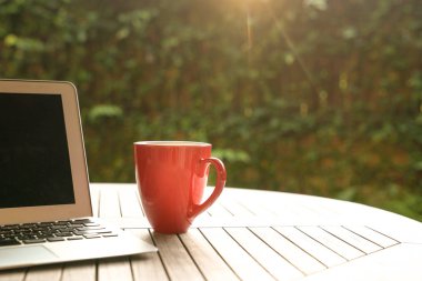 İş kavramı: Laptop ve Bahçe günbatımı sırasında yanında ahşap bir masa üzerinde kırmızı bir kupa
