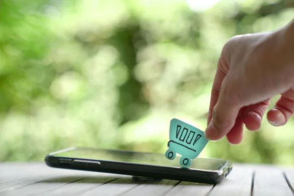 Online alışveriş veya e-ticaret kavramı: bir kağıt alışveriş sepeti üstünde tepe-in a acımak telefon