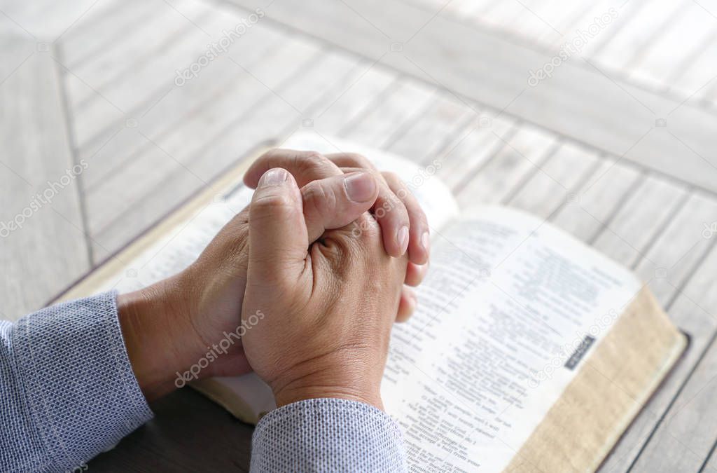 Praying: male hands clasped together on an old bible
