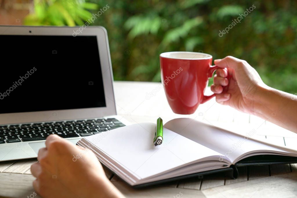 Work Concept: Hand on red mug with laptop and note pad and pen o