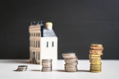 Savings concept: Coins stacked with a miniature house at the bac clipart