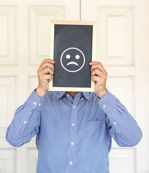 Emoticon triste na placa na frente da cara de um homem — Fotografia de Stock