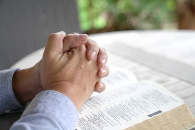 Praying : male hands clasped together on an open bible clipart