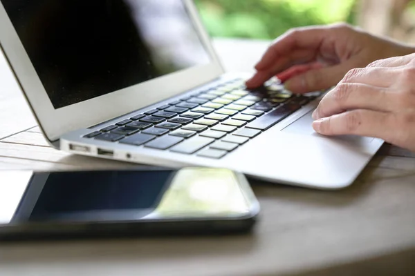 Hands typing on the keyboard of a laptop with cell phone next to — Stock Photo, Image