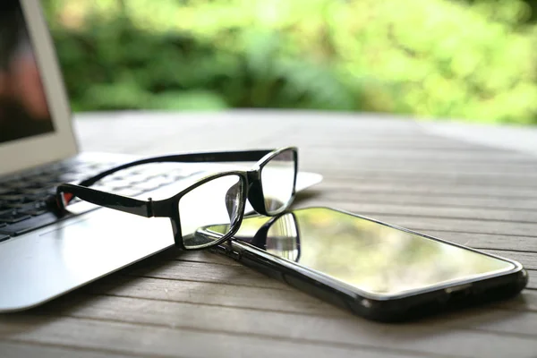 Laptop, Handy und Lesebrille auf einem Holztisch, — Stockfoto