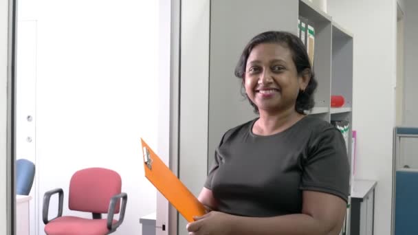 一个手里拿着文件的亚裔印度女商人在镜头前微笑的画像 工作场所设置 — 图库视频影像