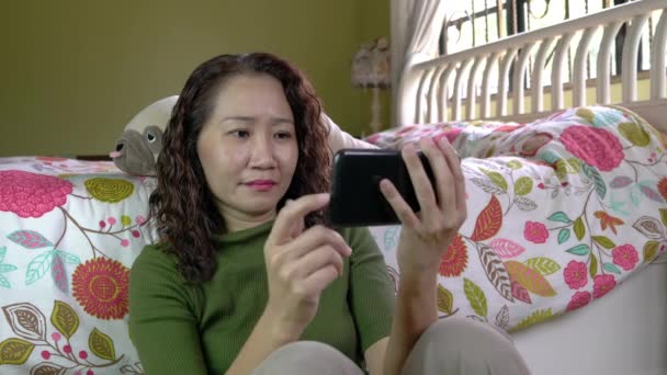 アジア系中国人のビジネスマンが寝室で携帯電話でビデオを見ている デジタルライフスタイル — ストック動画