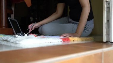 Evden ya da uzaktan çalışma konseptinden çalış. Yerde oturan bir kadın, not defterine ve bilgisayarına yazı yazıyor.. 