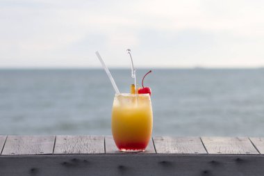 Glass of fruit punch or mocktail on wood top with ocean view clipart