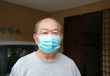 Evde tıbbi maskeli yaşlı bir adam var. Covid-19 riskini azaltmak için evde kalın..
