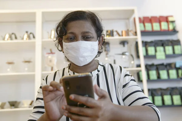 Indian woman with face covered with medical face mask reading her cellphone inside a restaurant.