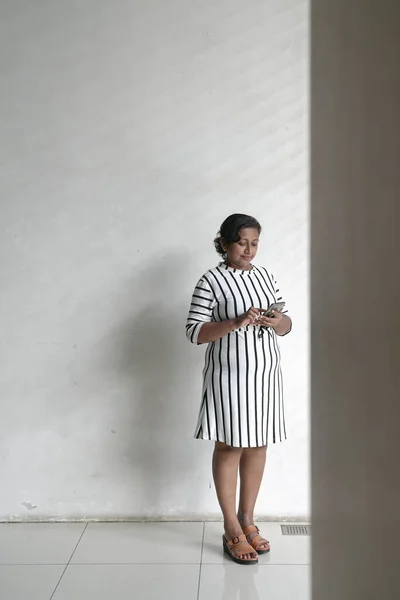 Indian corporate woman standing next to a white wall surfing her cellphone. Copy space.