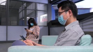 İki kişi, bir kız ve yüz maskesi takan bir adam cep telefonuyla yan yana oturuyor. Sosyal uzaklık, Covid-19 veya Coronavirus 'a karşı önlem olarak yeni normal.