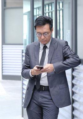 Çinli iş adamı takım elbiseli ve kravatlı, cep telefonunu kullanıyor..