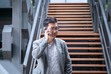 Çinli işadamı merdivenin dibinde cep telefonuyla konuşuyor.