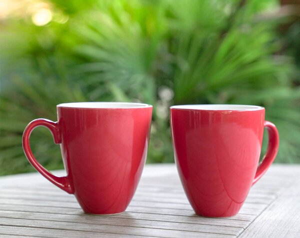 Две красные чашки на столе с зеленым фоном пальмы.