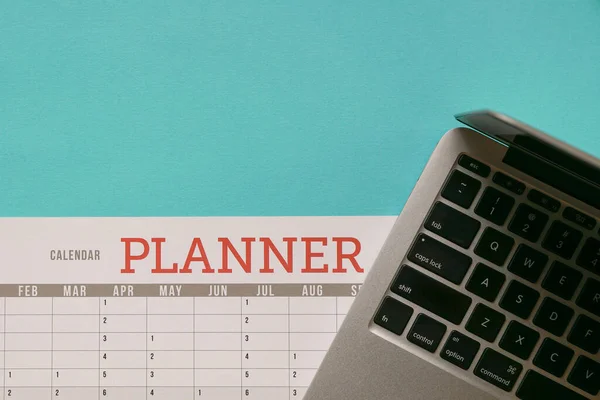 Computer laptop on top of calendar planner and blue tabletop. Business planning concept.