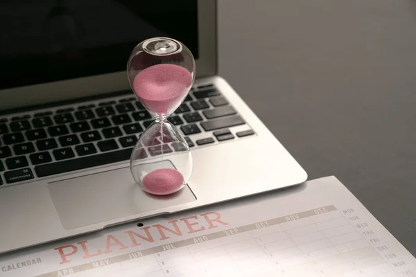 Hourglass on top of computer laptop and calendar planner. Business planning concept.