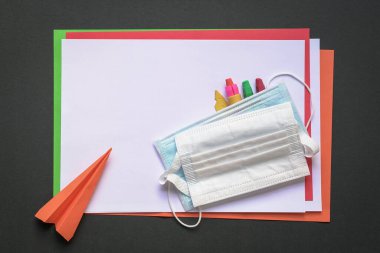 Renkli kağıtlar, boya kalemleri, kağıt uçak ve tıbbi maske. Üst Manzara. Covid-19 konsepti sırasında okula dönmek.