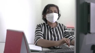 Bilgisayar klavyesinde yüz maskesi takan bir kadın. Coronavirus salgını sırasında çalışma yeri. 