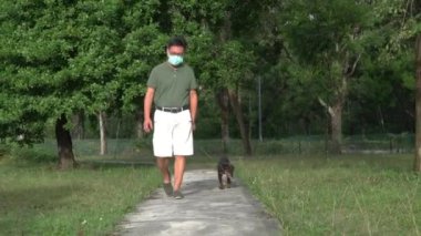 Parkta köpeğini gezdiren maskeli bir adam. Salgın sırasında evcil köpekle açık hava egzersizi..