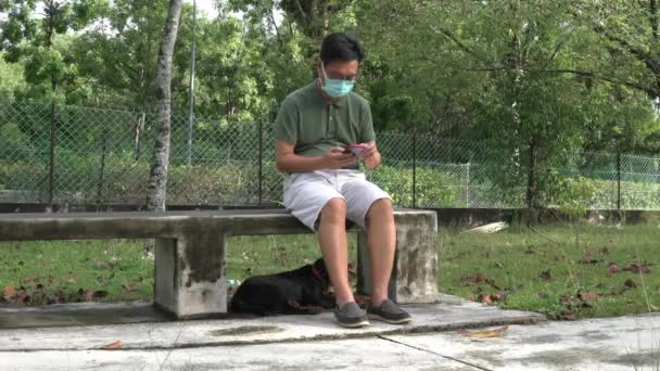 Muž Obličejovou Maskou Sedící Lavičce Čtoucí Mobilu Psem Nohou Čas — Stock video