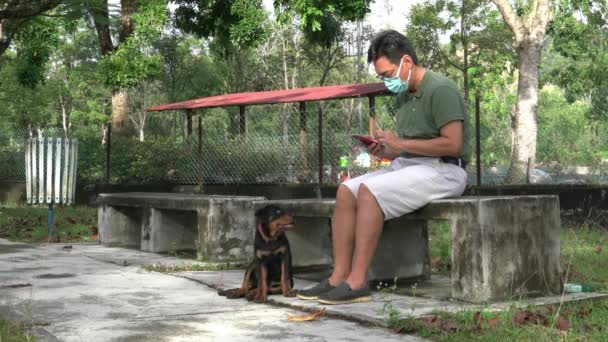 Hombre Con Máscara Facial Sentado Banco Leyendo Celular Con Perro — Vídeos de Stock