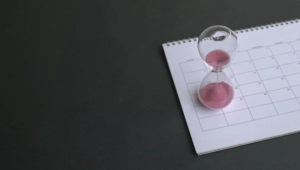 Hourglass with sand flowing, on top of calendar. Black top background.