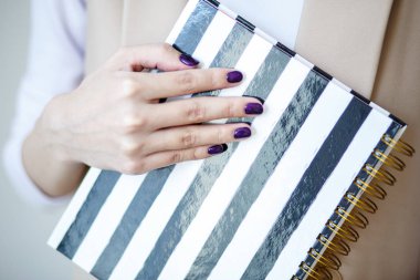 Yakın çekim fotoğraf manikürlü kadının el Siyah beyaz şeritler ile şık bir defter tutmak. Mor oje