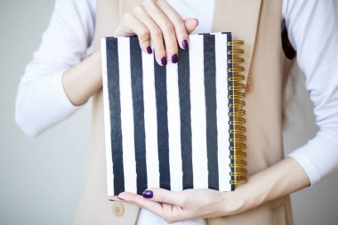 Yakın çekim fotoğraf manikürlü kadının el Siyah beyaz şeritler ile şık bir defter tutmak. Mor oje
