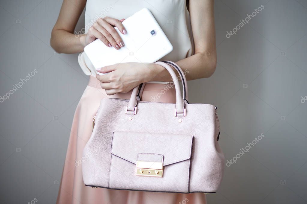 Digital electronic tablet on a woman's hands. Leather light pink handbag, summer elegant style