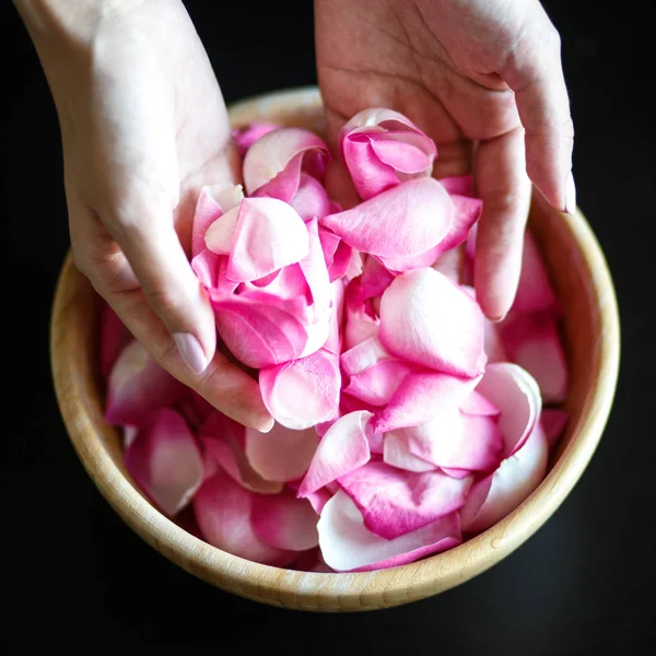 Yakın çekim makro fotoğraf siyah bir masada ahşap kase kadının el ile gül yaprakları,