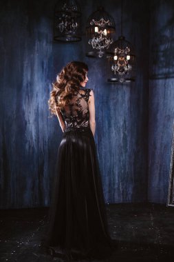 Uzun kıvırcık saç ve makyaj uzun lüks abiye, içinde olan genç kadın iç karanlık bir odada poz. moda güzellik portresi