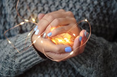 Güzel manikür, pastel ihale renk oje, closeup fotoğraf. Noel ışık çelenk üzerinde gri arka plan örgü kadın el ele tutuşur