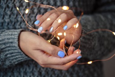 Güzel manikür, pastel ihale renk oje, closeup fotoğraf. Noel ışık çelenk üzerinde gri arka plan örgü kadın el ele tutuşur