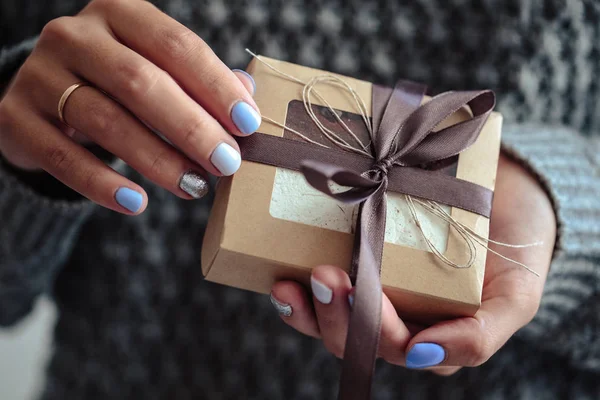 Gorgeous manicure, pastel tender color nail polish, closeup photo. Female hands hold a simple gifts over knit grey background